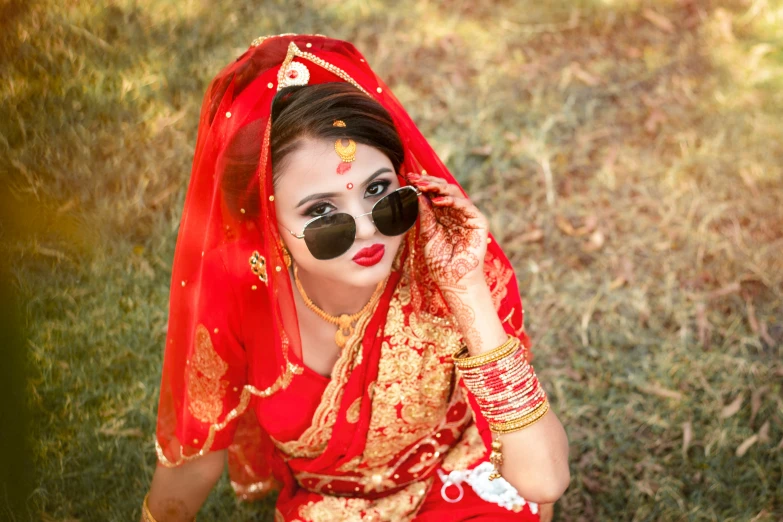 a woman wearing a red sari and orange accessories with black and white sunglasses and matching fake fur