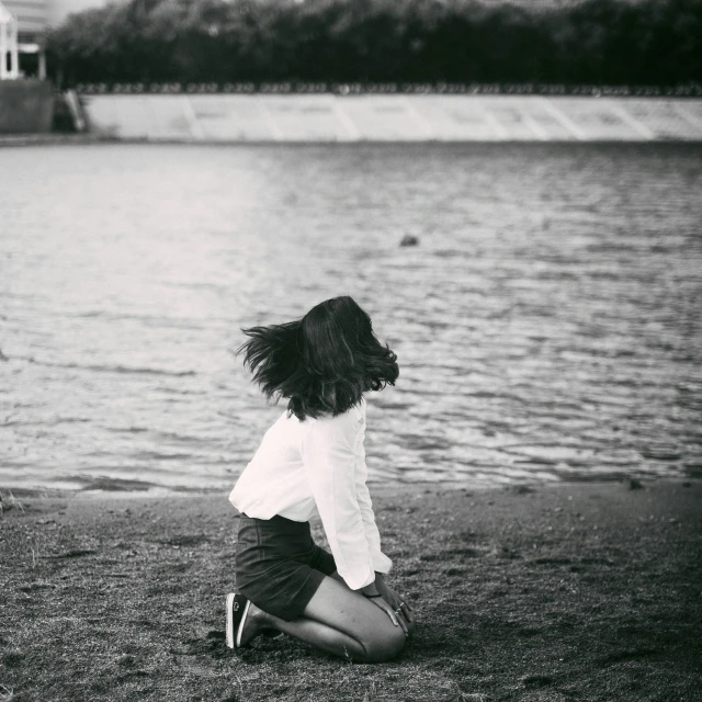 a black and white pograph of a girl kneeling by the water