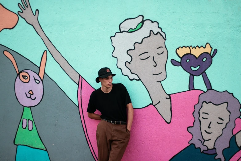 a man leans against a colorful wall with images of people on it