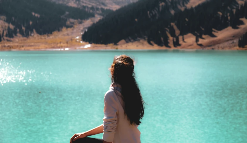 a woman that is sitting on a bench in front of a lake