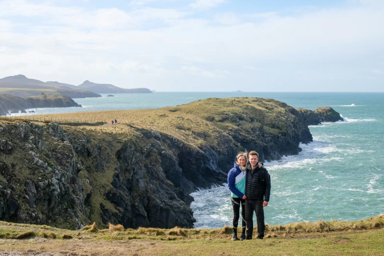 two people standing on the edge of the cliff looking out over the water