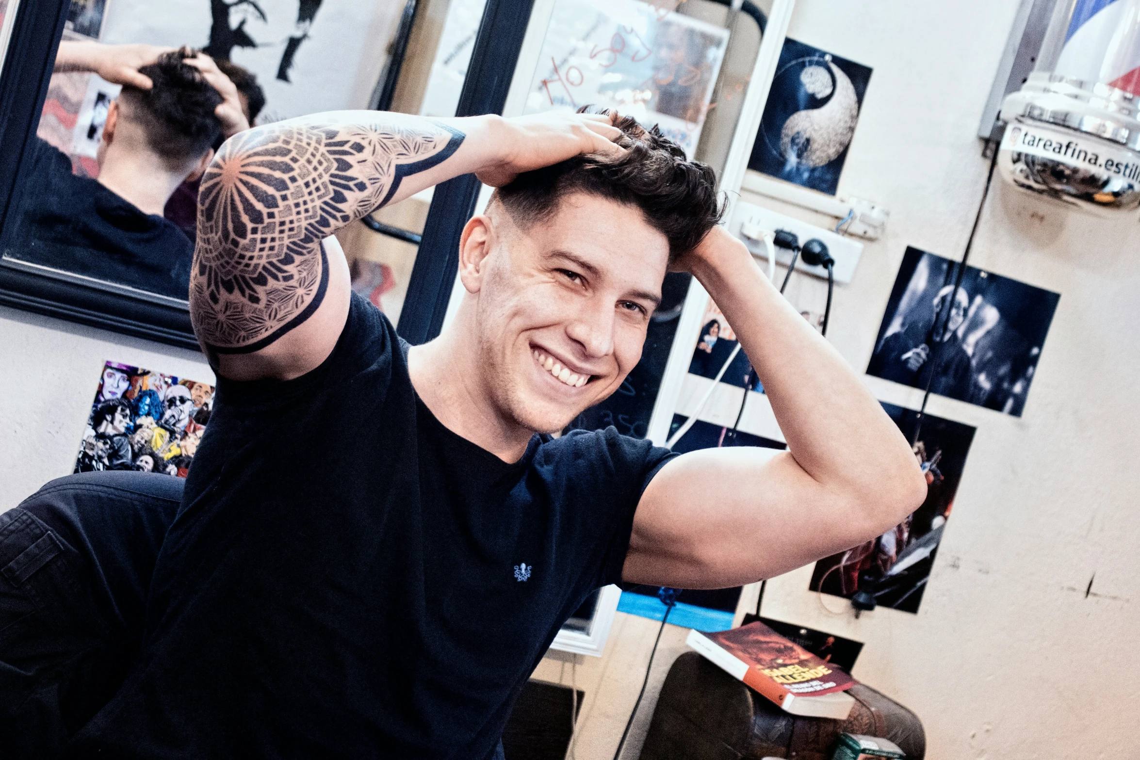 a man with tattoos, smiles while posing in his hair salon