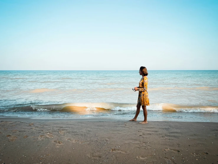 a girl in a yellow dress stands at the edge of the water