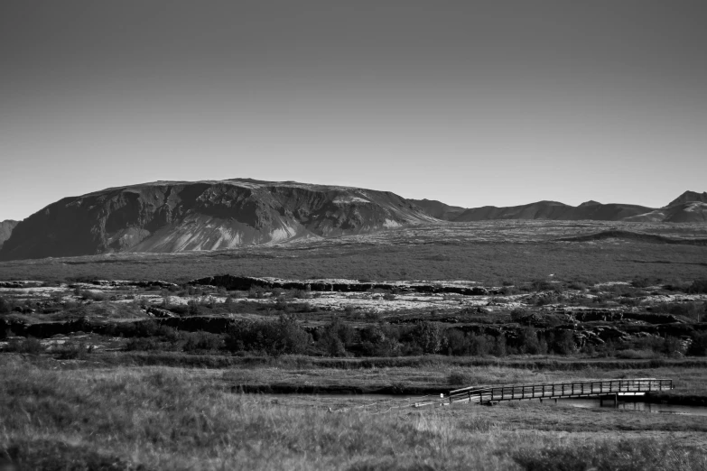 a bridge across the field in front of a big mountain