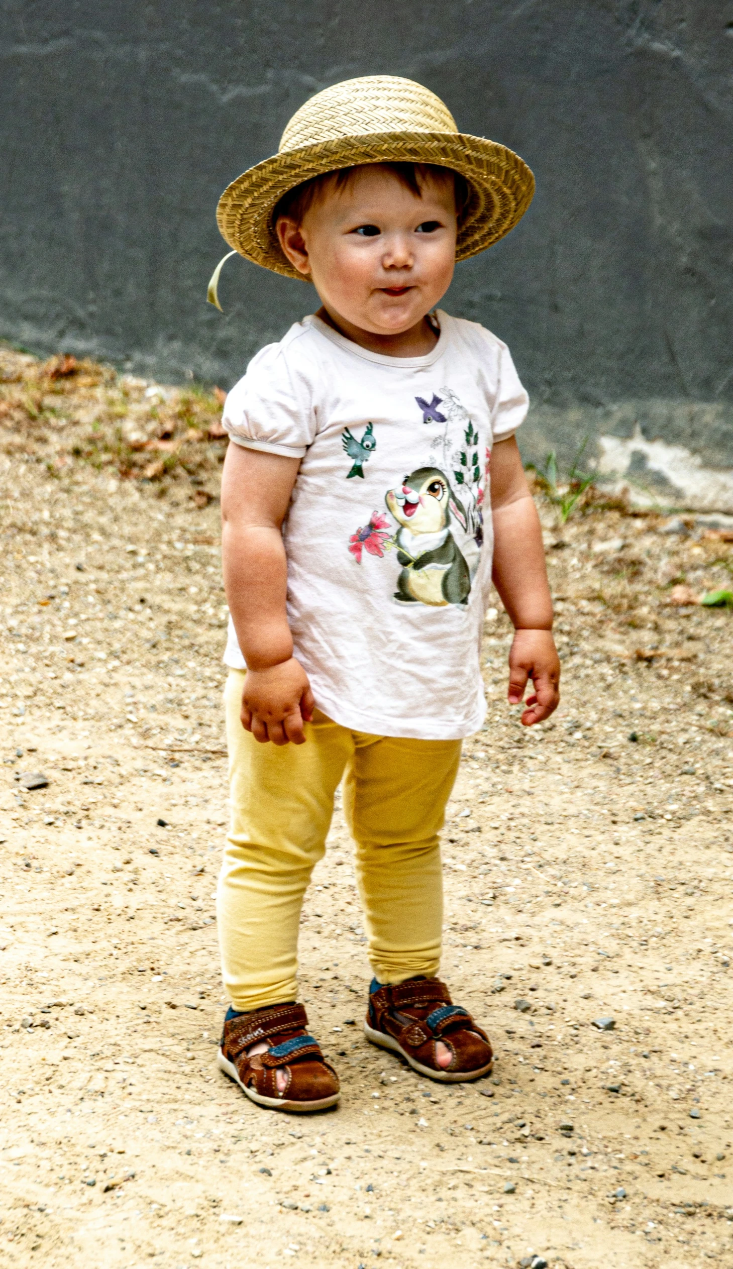 a little boy wearing a straw hat standing on a dirt field