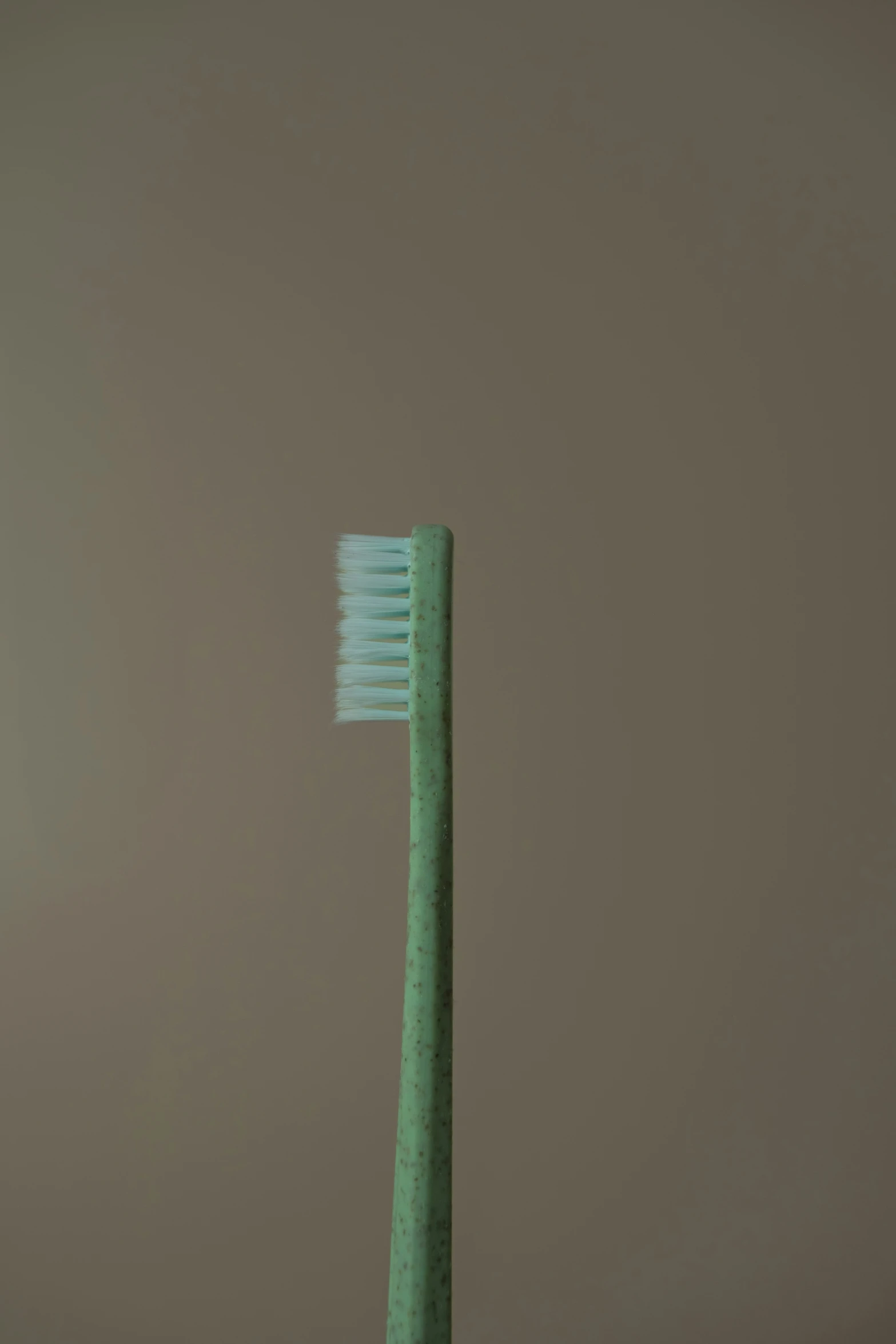 the green toothbrush is against the beige wall