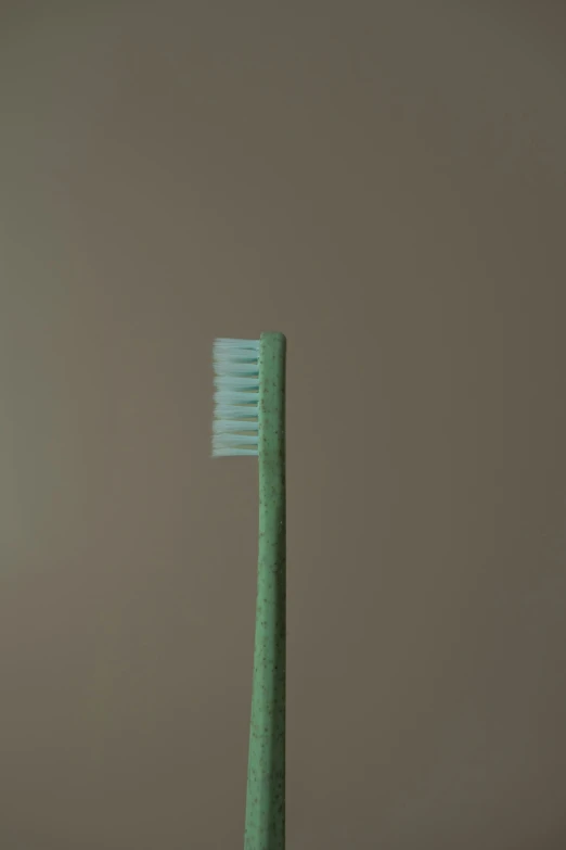the green toothbrush is against the beige wall
