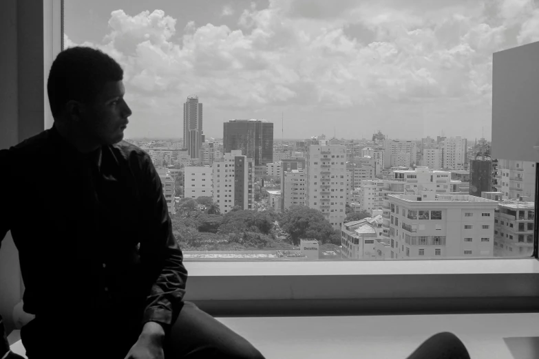 a person sitting in front of a window with city buildings behind him