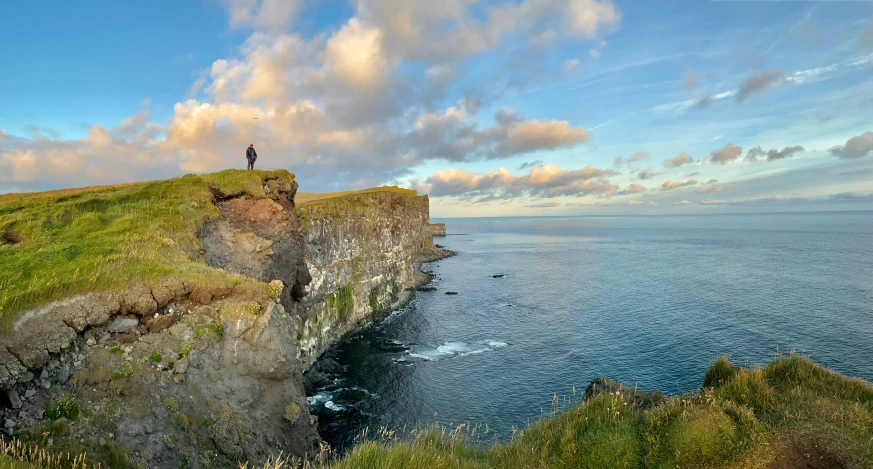 a man standing on a grassy mountain next to the ocean