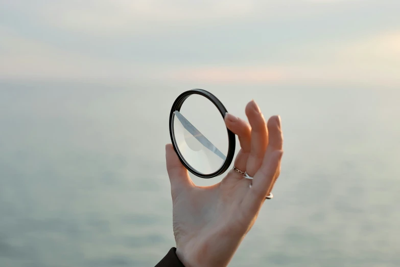 a hand holding a small black ring over the water