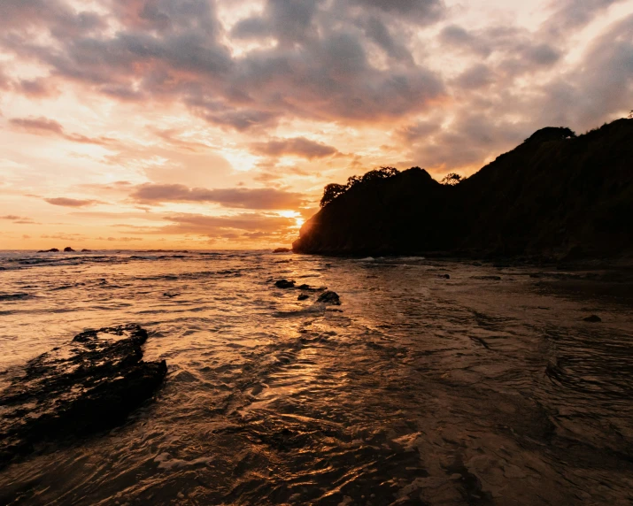 sunset at the shore of a beach near a rocky mountain