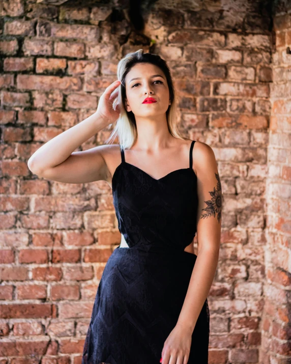 a young woman in a black dress posing against a brick wall