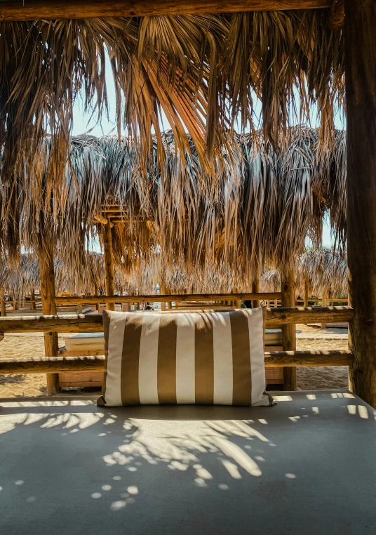 a white and beige striped pillow sitting on a wooden bench