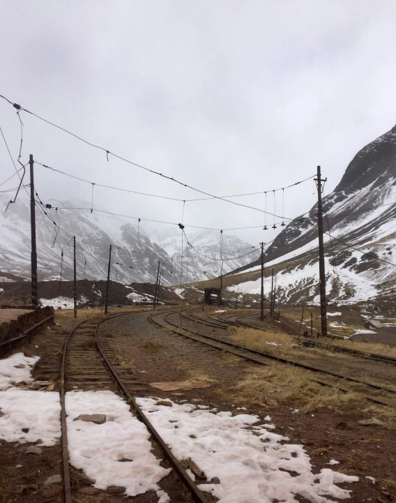 several rail lines with electric poles, snow and mountains