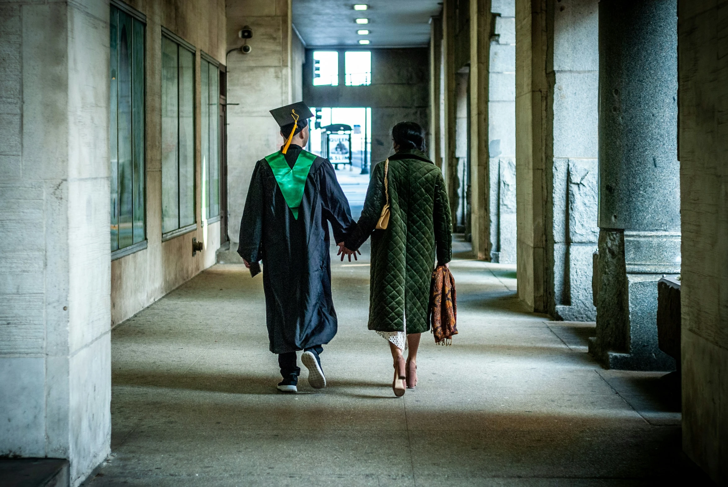 two people walking down a building with a green graduation hat