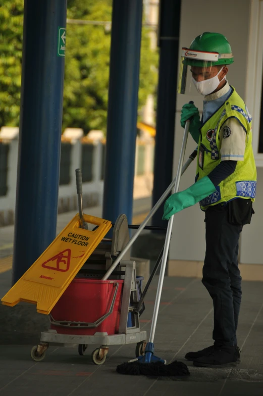 a man in a green safety vest and face mask cleaning with h cart