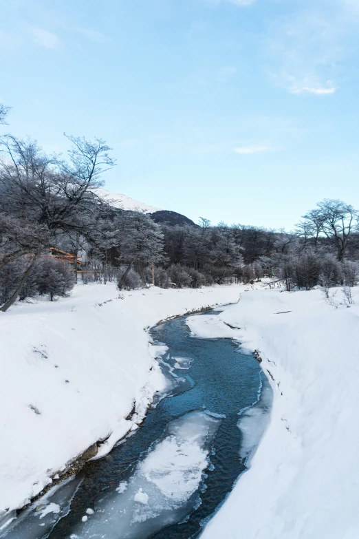 a snowy stream with blue water near the snow