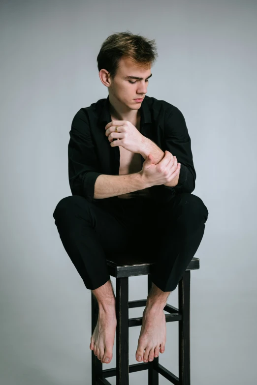 a young man sitting on a stool in front of a gray background