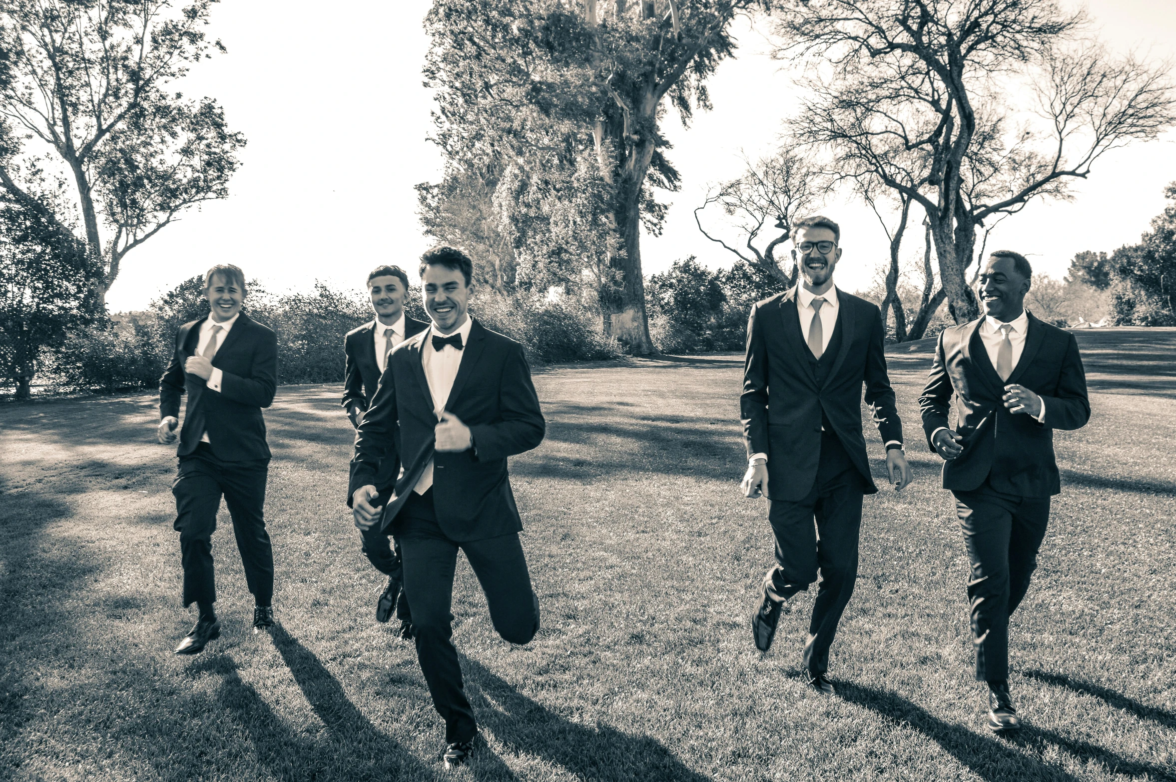 three men dressed in suits and ties running across a grass field