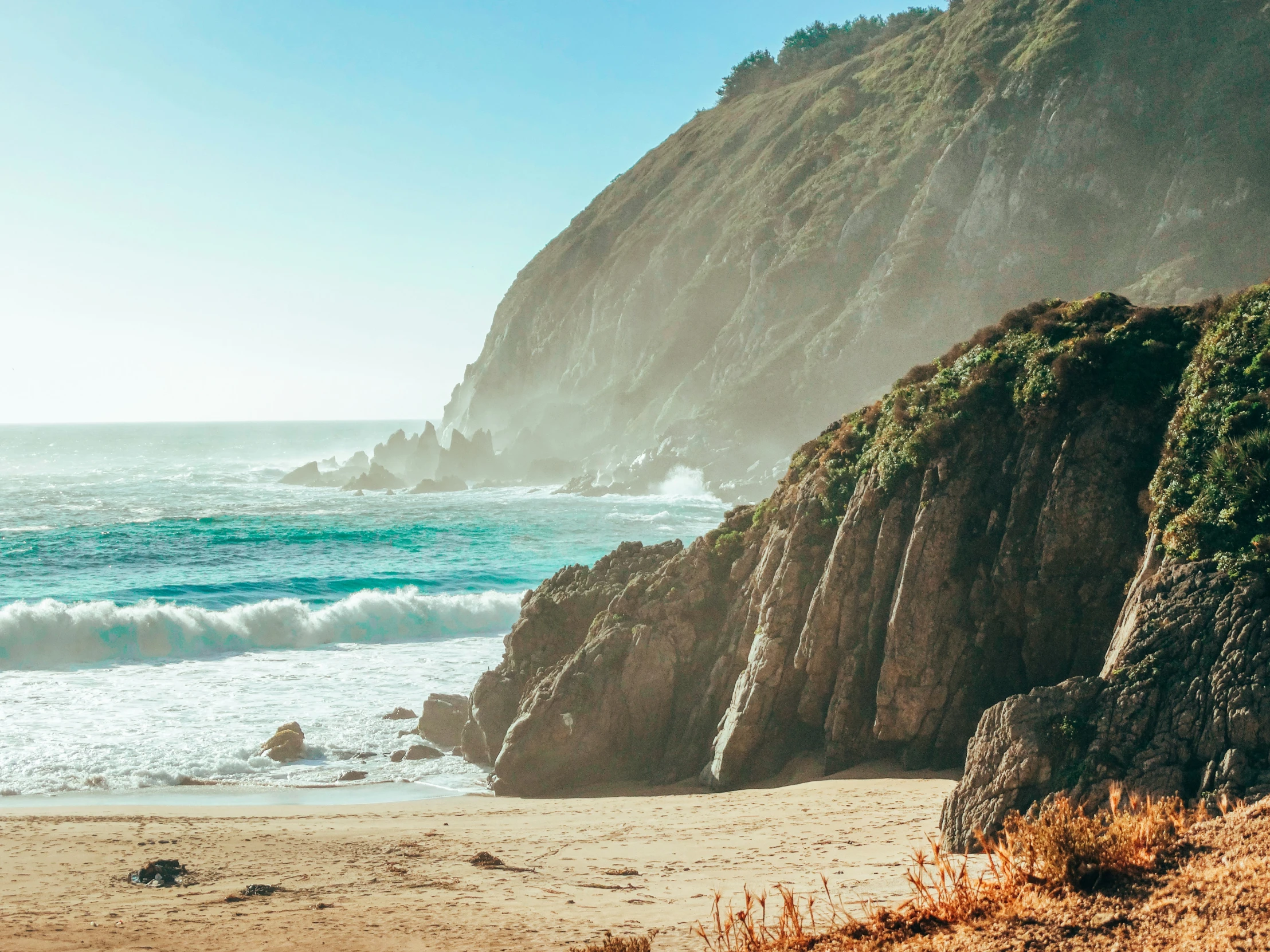 a sandy beach with two rocky cliffs on either side and a few waves in the ocean