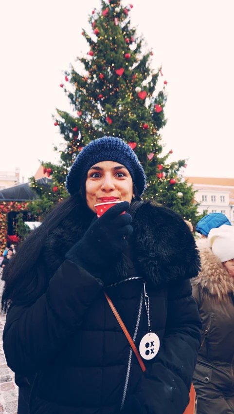 a woman standing in front of a christmas tree wearing a black puffy coat