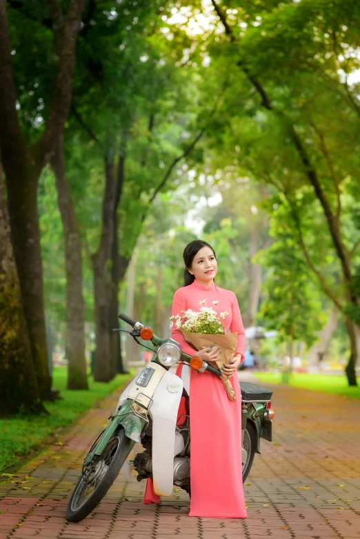 a woman wearing an orange dress holding flowers next to a scooter