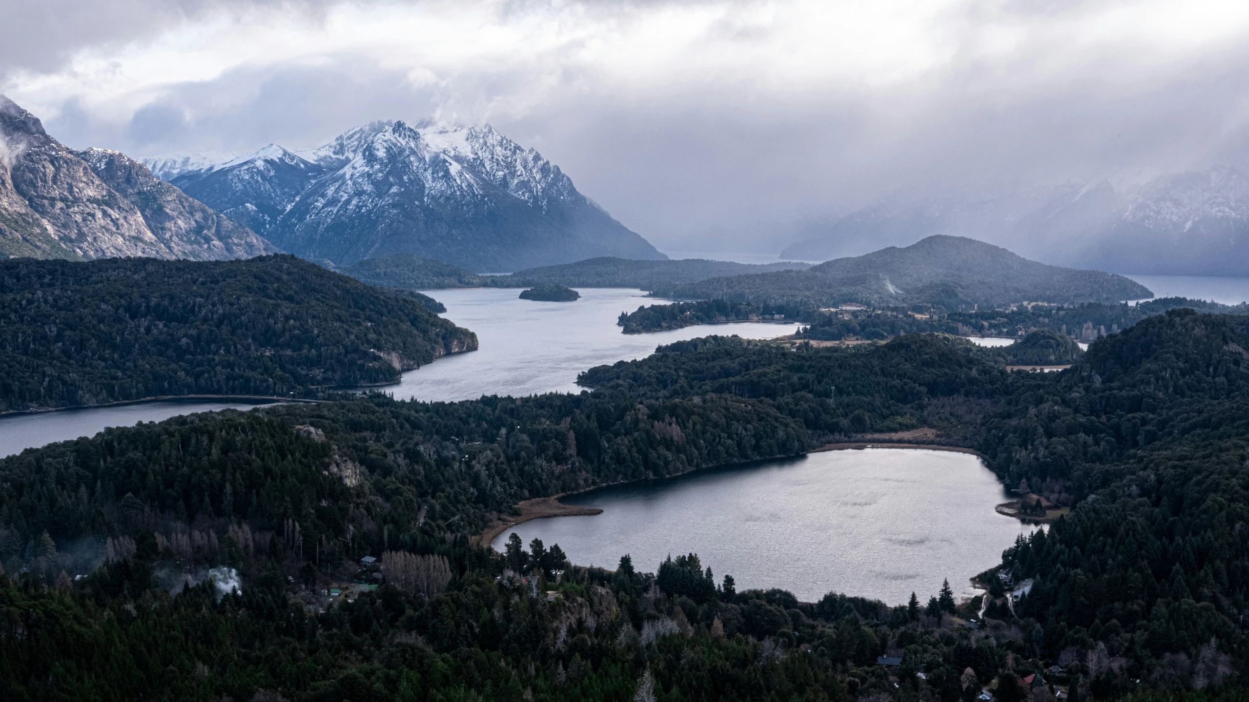 snow - capped mountains surround a lake with small, evergreen trees