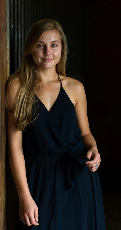 a woman standing by a wall in a black dress