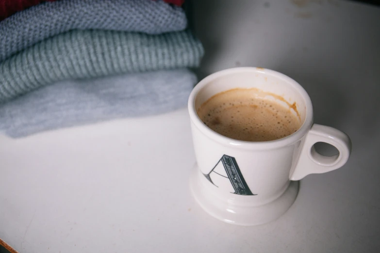 cup of coffee sitting on a table next to pile of folded clothes