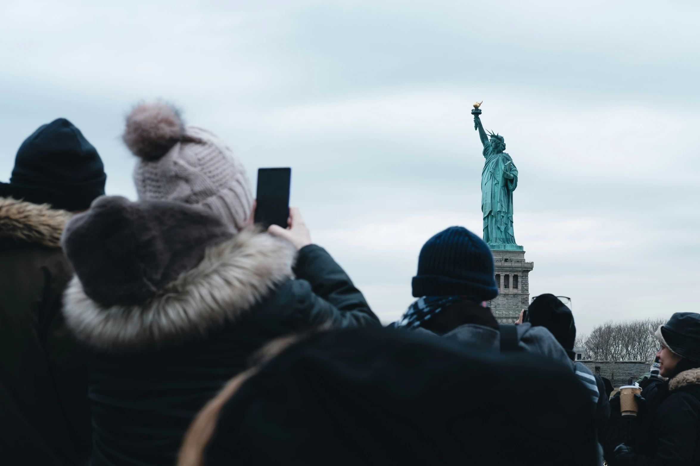 a woman taking a picture with her cell phone of the statue of liberty