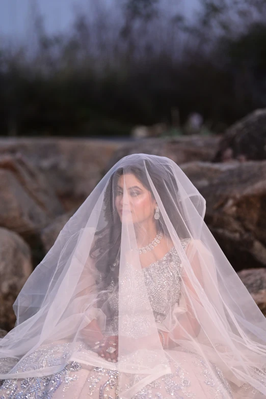 a woman sitting on a rock with a veil over her head