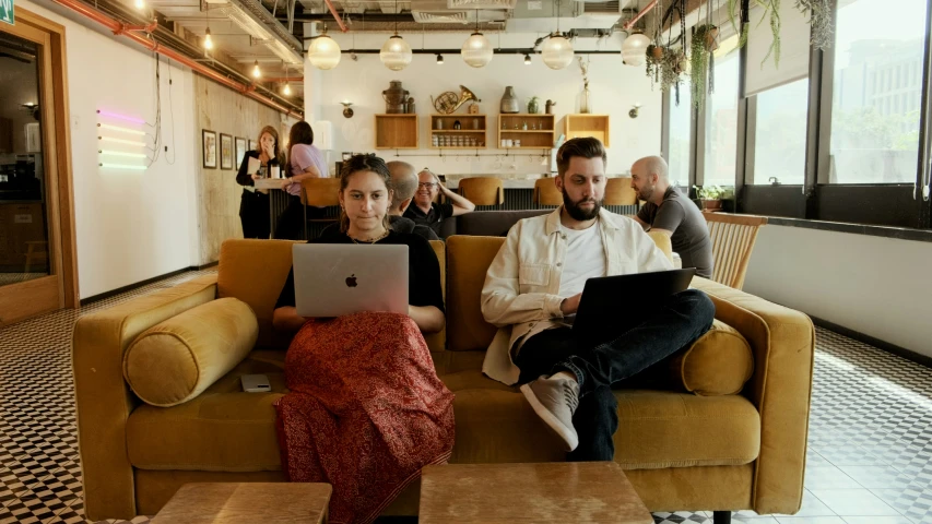 two men sit on the couch with their laptops