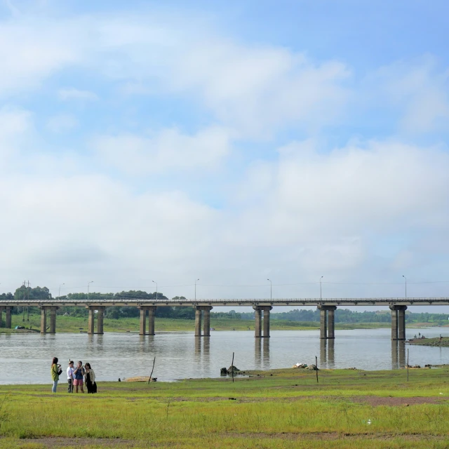 a group of people standing by the water and bridge