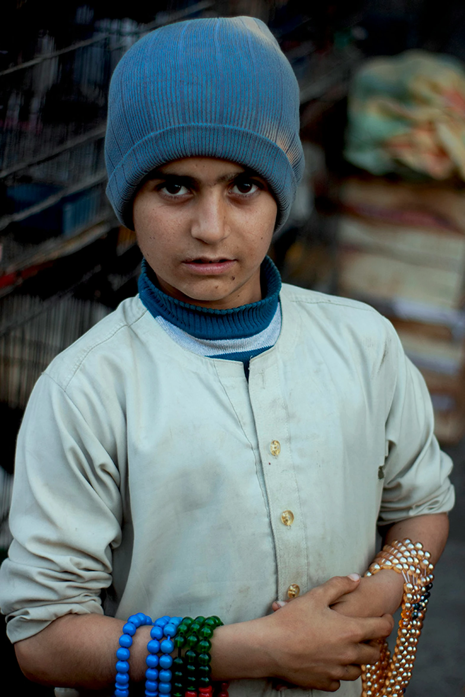 young man with a blue hat, celets and a jacket standing outdoors