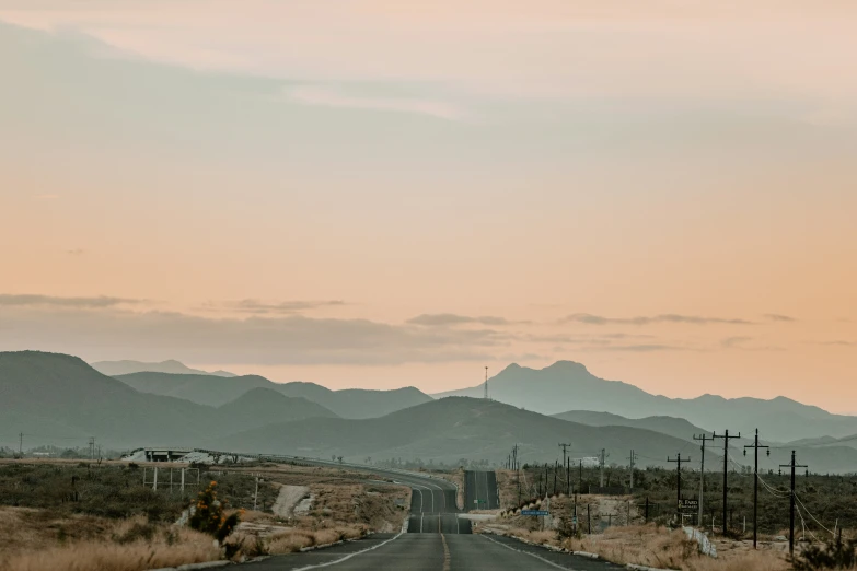 an empty road in the middle of the desert with mountains on one side and telephone poles and telephone poles on the other side