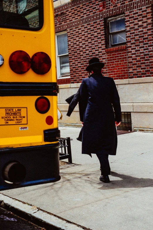 the woman is wearing a black coat and walking towards the yellow school bus