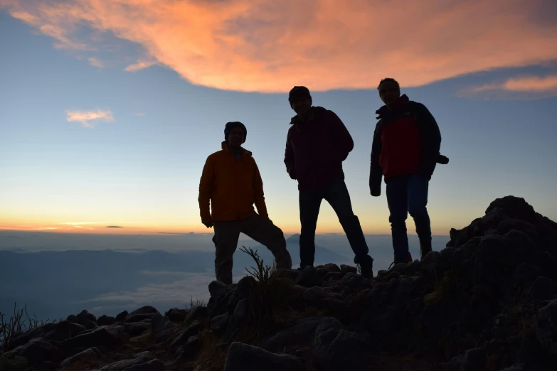 three people standing on top of a hill in the sunset