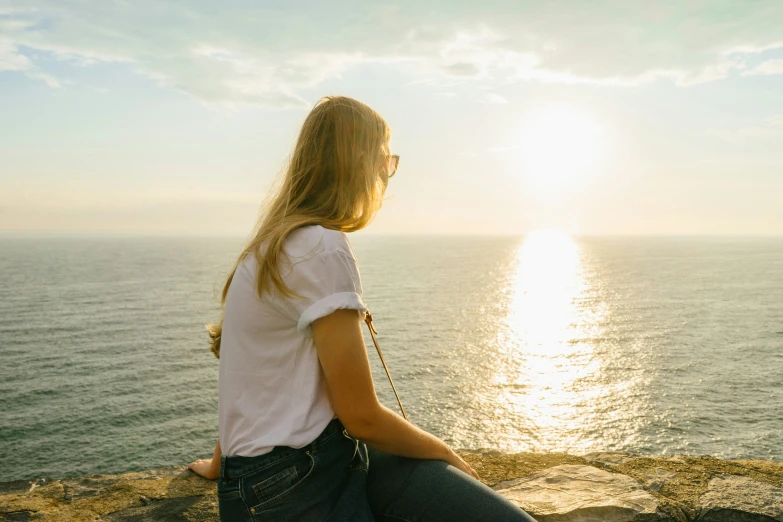 the woman is sitting on a rock looking out into the water