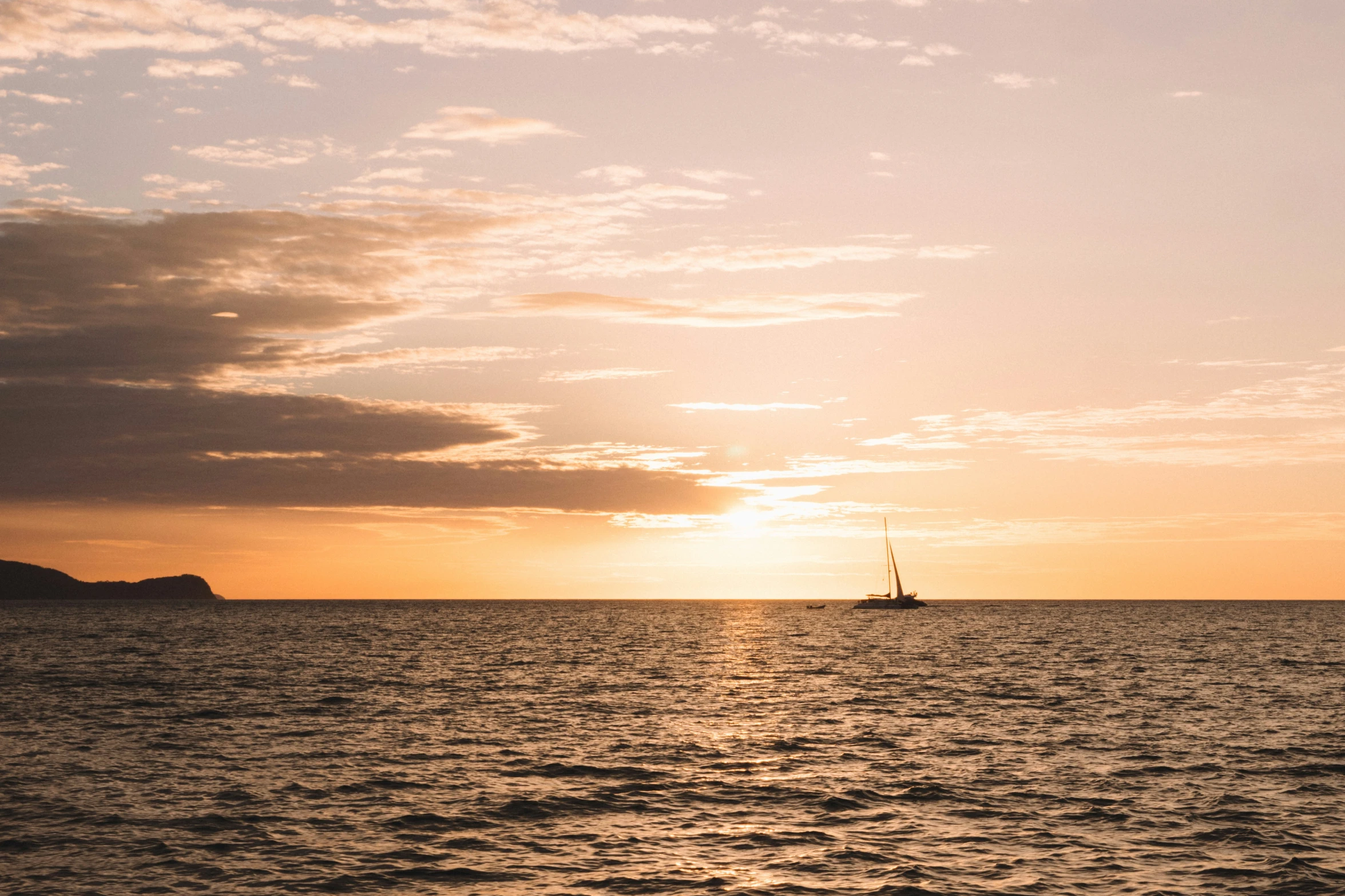 a sailboat sailing across the ocean at sunset