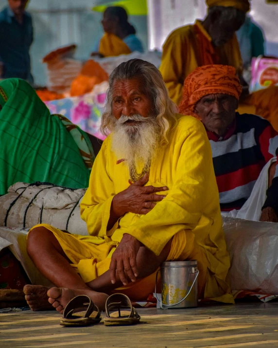 an elderly man with long white beard and bright yellow dress is sitting in the middle of the street