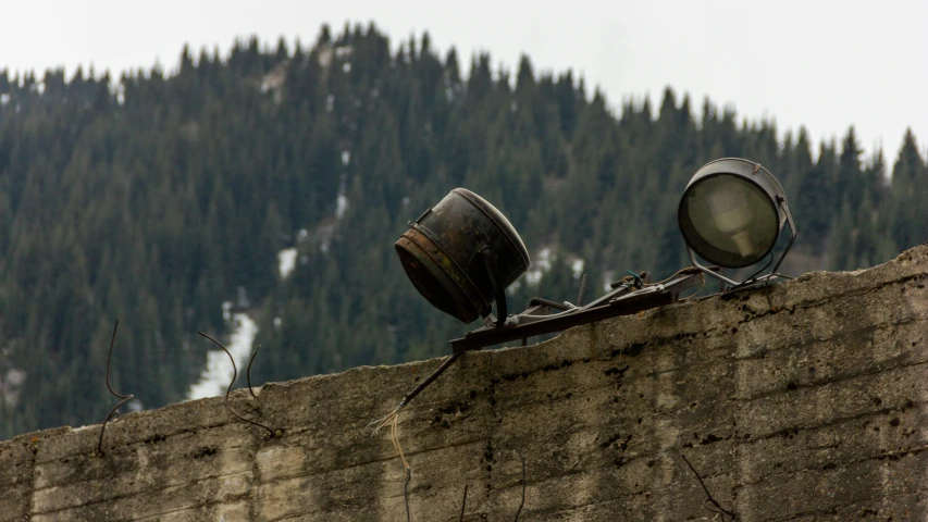 two lights on top of a stone wall by a forest