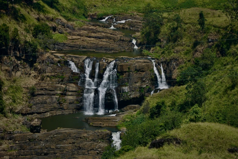 two horses stand near a waterfall while some people look on