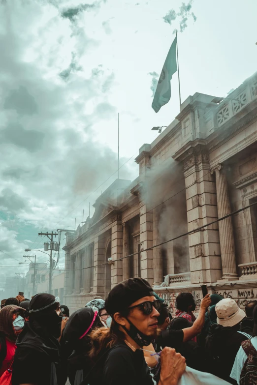 group of people in front of large building while smoke billows from it