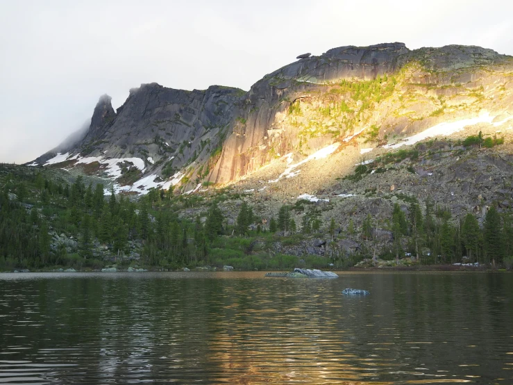 a mountain near water and trees with low sunlight on the top