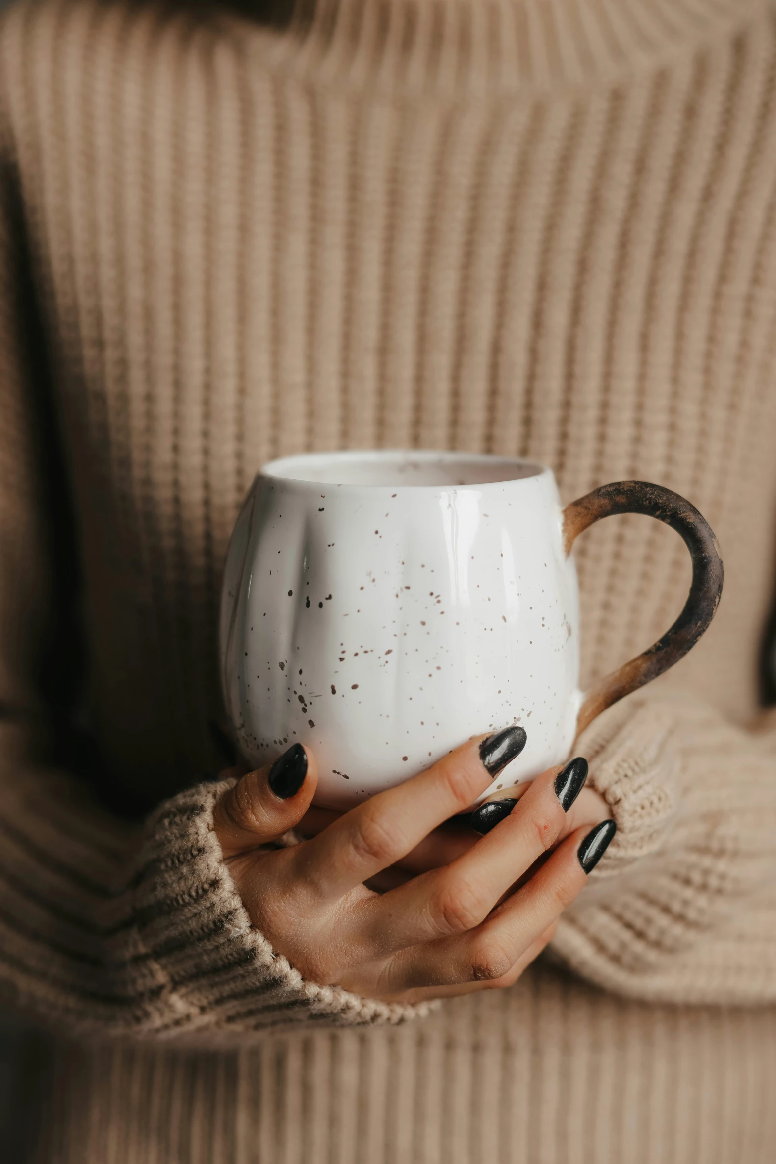 woman holding mug in hands against beige jumper