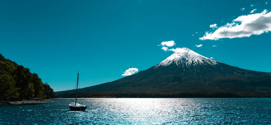 a sail boat sailing on a lake front to a snow covered mountain