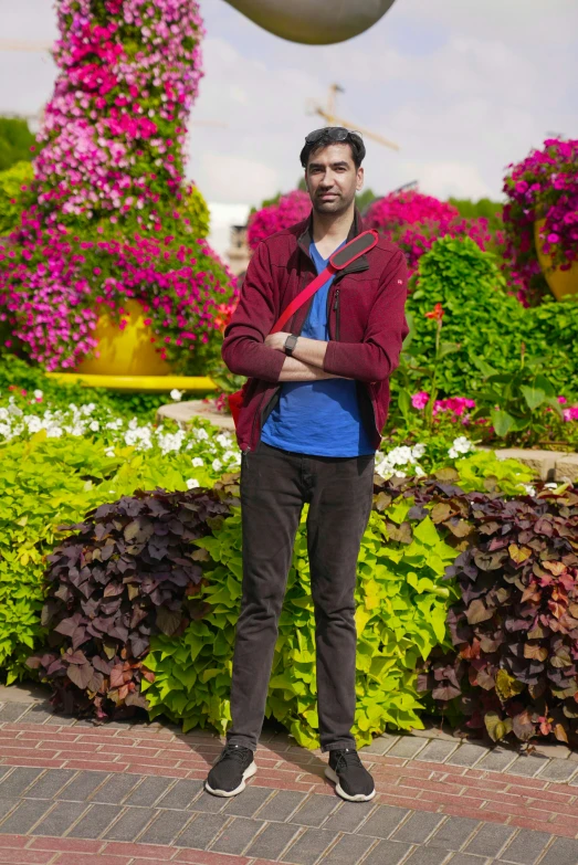 man standing outside with his arms crossed and flower garden behind him