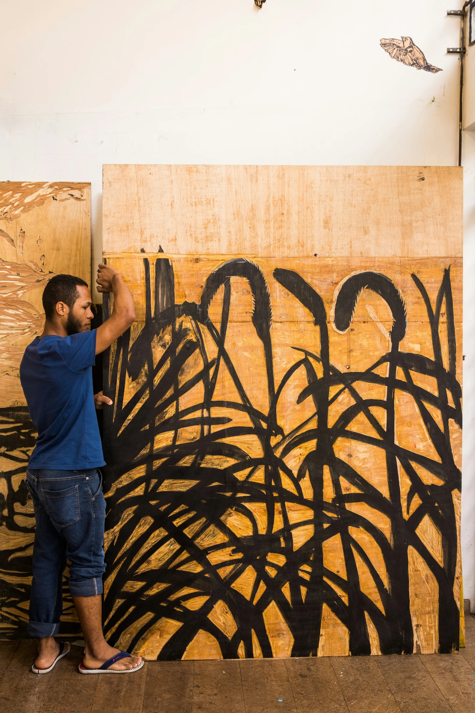 a man in blue shirt painting on canvas next to large tree