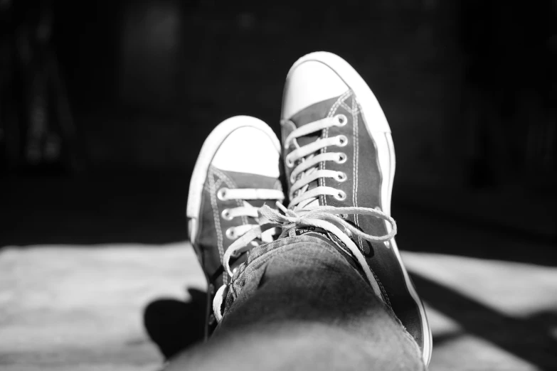 a black and white pograph of feet with converse shoes on