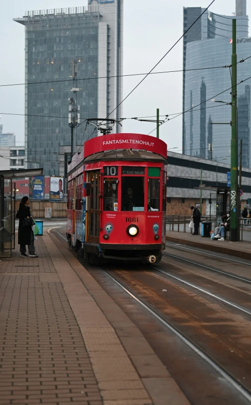 a red tram is going down the track with other people standing on it